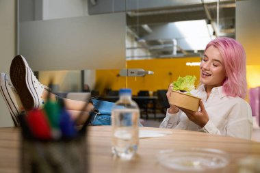 Mutlu bayan masada oturuyor, elinde sağlıklı vejetaryen yemeği ve eko tabağı tutuyor.