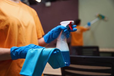 Cropped photo of cleaner wearing gloves and holding spray bottle and cloth for wiping clipart