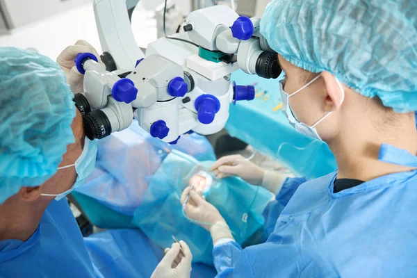 Cirurgiões Proteção Máscara Chapéu Olhando Microscópio Cirúrgico Paciente — Fotografia de Stock