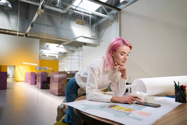 年轻的粉红头发设计师坐在桌旁 一边做着同事间的建筑项目 — 图库照片