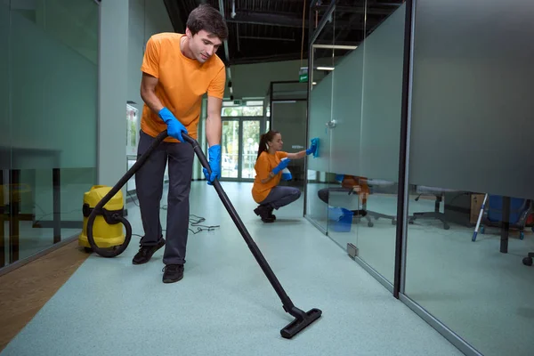 彼の同僚は 建物内のガラスの表面を掃除しながら 若い男は床を真空 — ストック写真
