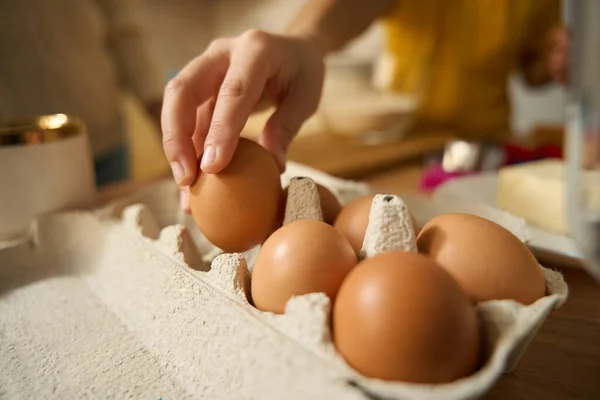 Close up photo of boy standing near table in kitchen and taking chicken egg