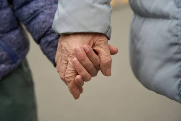 Close up photo of old lady and young boy in winter clothes holding hands of each other