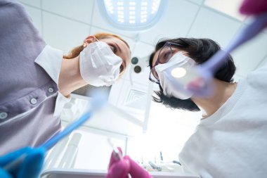 Diş manipülasyonu sürecinde olan iki tıp çalışanı özel aletler kullanır.