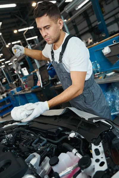 Male in protective suit and gloves standing near the car with open hood perform engine oil change
