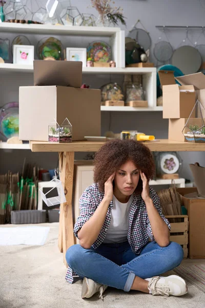 年轻的女性在她的礼品店的地板上坐着 工作一天后感到很疲倦 — 图库照片