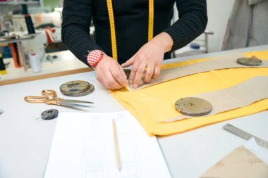 Siyah kazaklı terzi bir şablon çiziyor, terzi aletleri masanın üstünde.