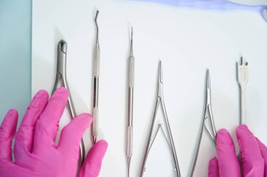 Dişçi metal aletler hafif bir yüzeyde yatar, doktor koruyucu eldivenlerle dokunur.