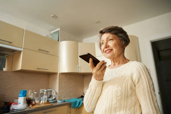 Ηλικιωμένη Γυναίκα Γυαλιά Στέκεται Στην Κουζίνα Κρατώντας Smartphone Και Έχοντας — Φωτογραφία Αρχείου