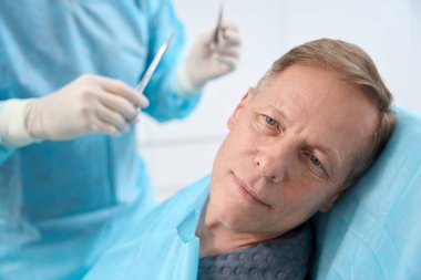 Doktorun ona dikiş atmaya hazırlanırken sakin görünen orta yaşlı bir adamın yakın plan fotoğrafı.