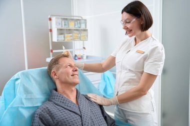 Koruyucu gözlük konusunda başarılı bir kadın sağlık uzmanı elinde şırıngayla hastasıyla prosedür boyunca konuşuyor.