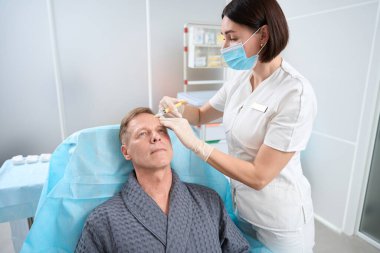 Orta yaşlı bir adam modern klinikteki profesyonel bir doktordan cilt gençleştirme için plazma enjeksiyonu alıyor.