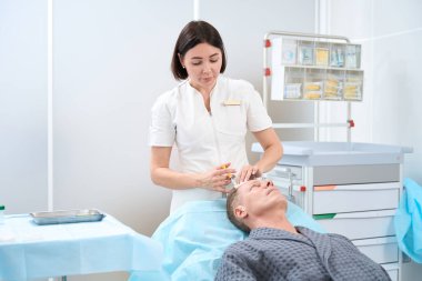 Beyaz üniformalı nitelikli kozmetik uzmanı yaslanmış koltukta yatan bir adam için trombosit zengini plazma enjeksiyonu yapıyor.