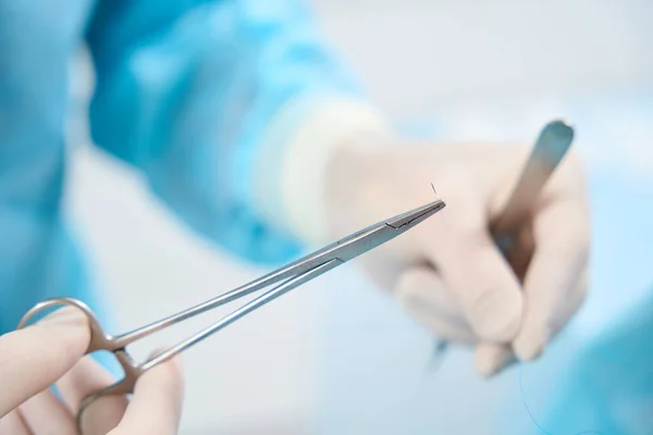 Close-up photo of medical needle and thread in hands of a medical professional preparing to put stitches on patient