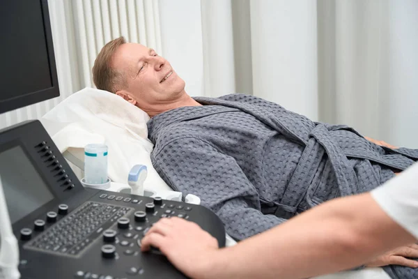 Middle-aged calm man lies on a couch in the ultrasound room, next to the doctor