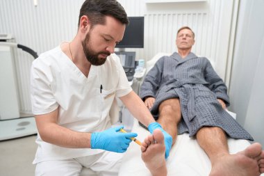 Ciddi bir tıp doktoru, biyopsi analizi için hastanın ayak bileğinden hücre örneği alıyor.