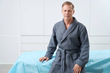 Gülümseyen orta yaşlı hasta yatakta oturuyor, o parlak bir odada.