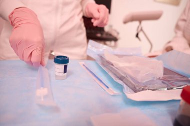 Tıbbi giysili ve koruyucu eldivenli kadın doktor elinde tıbbi aletlerle masanın yanında duruyor ve bir tane alıyor.