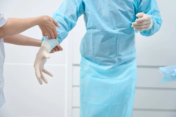 Cropped photo of medical staff in full-body sterile gown having their hands inserted into surgical gloves