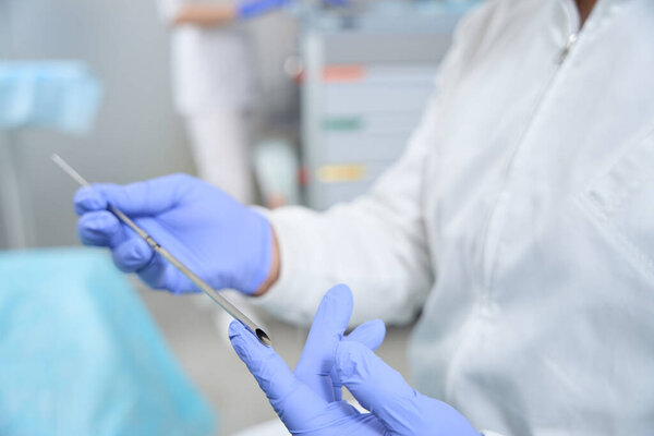 Doctor holds in his hands special tool for the installation of bioidentical hormones to patients, in the background an assistant