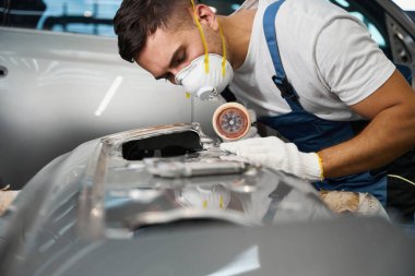 Araba tamponunun yanında duran ve özel makineyle boyaları söken takım elbiseli profesyonel bir adam.