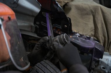 Koruyucu kasklı bir erkek, giysi ve eldivenler elinde metal bir alet, arabanın detaylarını kontrol ediyor.