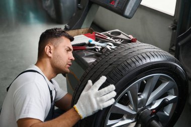 Koruyucu elbiseli ve eldivenli bir erkek direksiyona yakın duruyor ve garajda test ediyor.