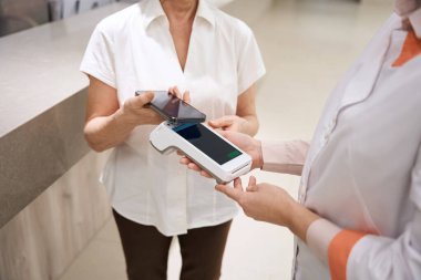 Patient pays for her visit to the therapist using the phone, the medical worker holds the terminal