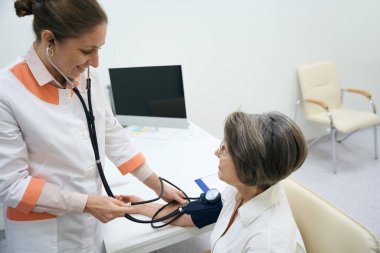 Smiling therapist measures the blood pressure of the patient with a tonometer, the doctor conducts a standard examination