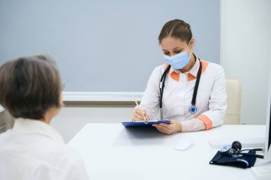 Therapist in a protective mask fixes the complaints of an elderly patient, women sit against each other