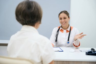 Friendly doctor conducts an appointment in the office, an elderly patient sits in front of her