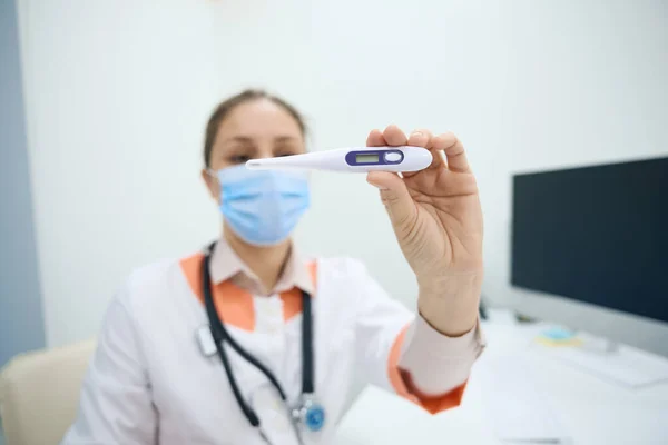 Woman medical worker holds a medical thermometer in her hands, she is in a bright office