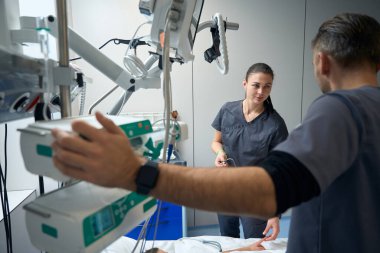 Patient lying on bed in ward, male and female doctor standing near and talking