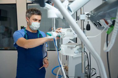 Doctor in protective mask standing in ward and checking information of patient health status