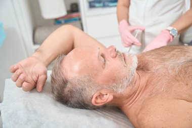 Dermatologist doctor makes injections from hyperhidrosis in the armpits to a patient, a man lies on a couch