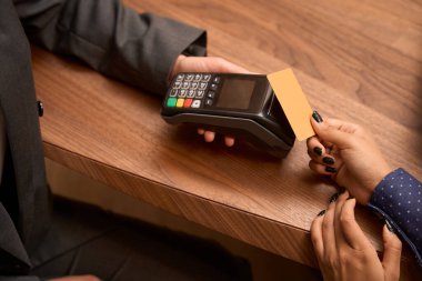 Close up photo of lady standing near the table and holding credit card, worker holding POS terminal