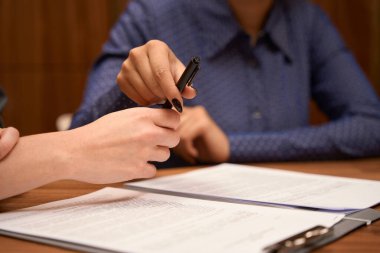 Female and administrators sitting by the table in cabinet, client signs contract