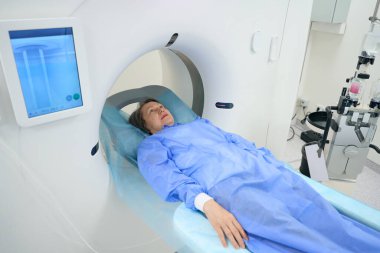 Woman undergoes a CT scan procedure in the diagnostic department of a hospital, she lies on a special mobile surface