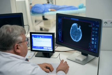 Elderly doctor performs MRI diagnostics of the brain in a modern clinic, patient lies in the tunnel of the apparatus