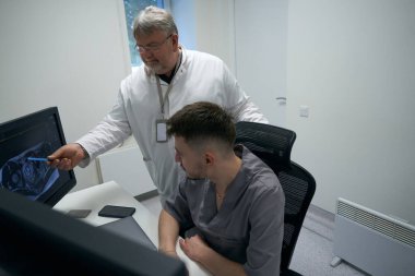 Two doctors are analyzing MRI results in a diagnostic room, they are using modern computers