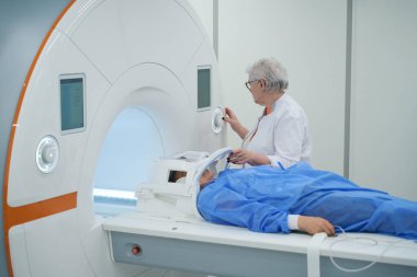 Doctor diagnostician sets up MRI machine to examine the patient, the woman lies on the moving part of the machine