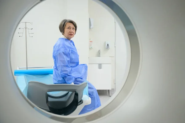 Woman looks into the camera of a modern CT machine, she is preparing for a diagnostic procedure