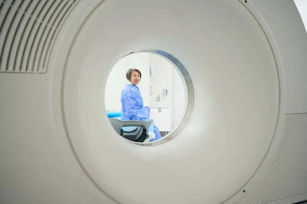 Elderly patient looks into the camera of a CT machine, she is preparing for a diagnostic procedure