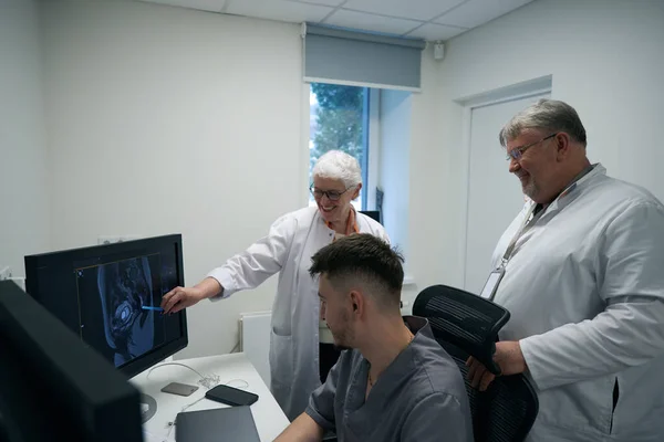 Employees of radiology, elderly woman and men, analyze the results of MRI diagnostics, colleagues are happy with positive dynamics recovery