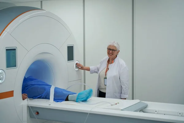 Elderly woman diagnostician performs an MRI procedure, the patient is in the chamber of the apparatus