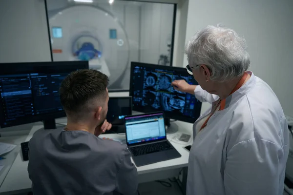 Doctors, a man and a woman, are looking through MRI images on a computer monitor, they are examining a patient