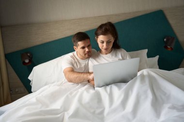 Guy and his girlfriend spend the morning together in bed, they read something in the laptop