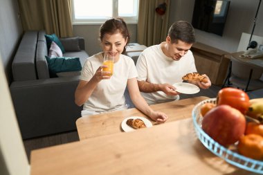 Man and a woman sit at a wooden table, they have breakfast with croissants and juice