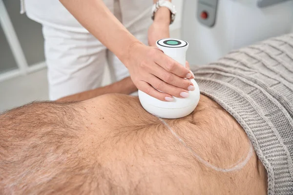 Body shaping specialist works with a patient in a specialized clinic, using modern equipment