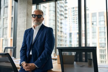 Committed middle-aged businessman standing in modern office building while looking at the camera